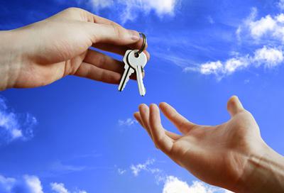 Keys to a house being passed from an agent to a buyer on moving day with a sky background 