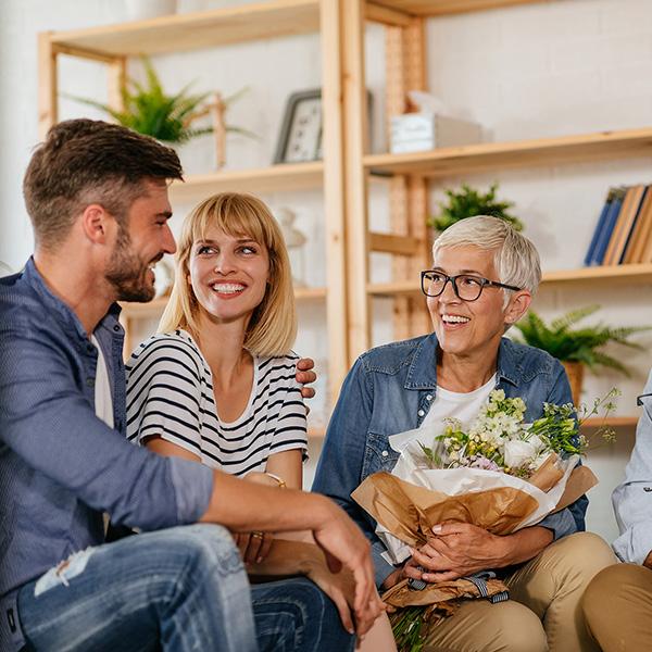 couple meeting with an elderly lady holding flowers in a living room smiling