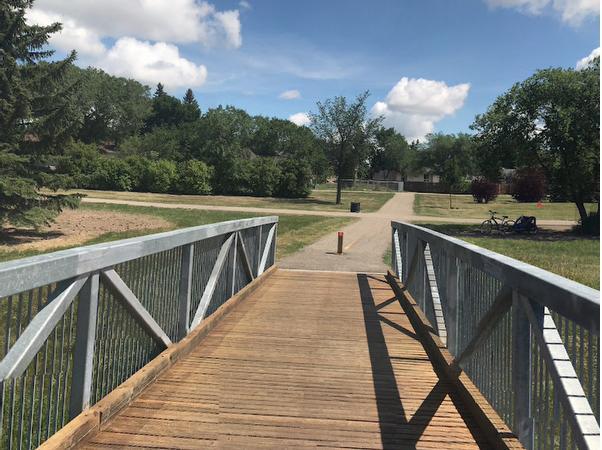 Bridge crossing the creek in Regina Normanview steel rails blue sky and green grass