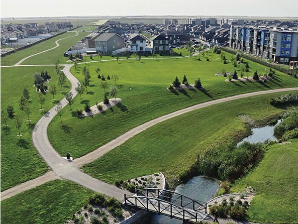 Bridge and walking bike paths surrounded by green grass tress with a large condo complex and  homes in the background 